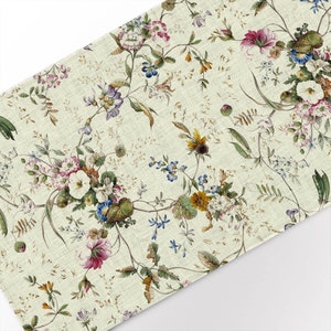 May include: A beige fabric with a floral pattern. The pattern features a variety of flowers in shades of pink, purple, blue, yellow, and green. The flowers are arranged in a repeating pattern.