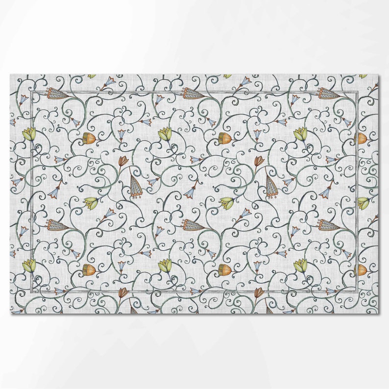 Puede incluir: Un mantel individual blanco con un patr&oacute;n repetitivo de dise&ntilde;os florales azules, verdes y naranjas sobre un fondo gris.