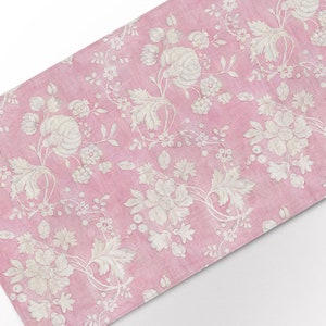 May include: A pink fabric table runner with a white floral pattern. The pattern features delicate flowers and leaves.