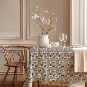 Può includere: Una tovaglia rettangolare con un motivo ripetuto di case multicolori e alberi di pino verdi su sfondo color crema. La tovaglia copre un tavolo apparecchiato con una brocca bianca contenente fiori bianchi, ciotole e due calici.