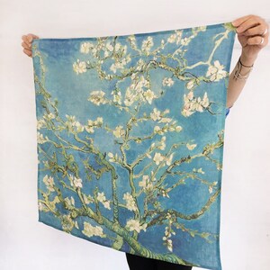 K&ouml;nnte beinhalten: Eine blaue und gr&uuml;ne Stoffwandteppich mit einem Gem&auml;lde eines bl&uuml;henden Mandelbaums mit wei&szlig;en Bl&uuml;ten vor blauem Himmel.