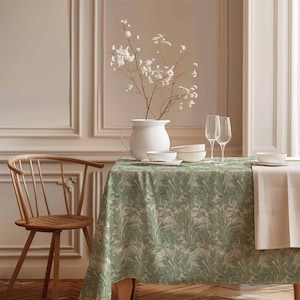 Pode incluir: Uma toalha de mesa verde com padrão floral, preparada para um jantar com duas taças de vinho, tigelas brancas e um jarro branco com flores brancas.