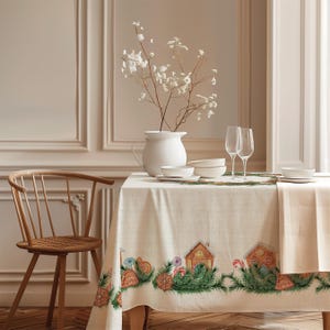 Puede incluir: Un mantel de color crema con un estampado de borde repetitivo de casas de jengibre, ramas de pino verdes y bastones de caramelo rojos y blancos. La mesa está puesta con una jarra de cerámica blanca, cuencos blancos y dos copas de cristal.