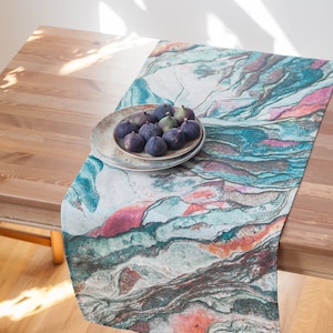 May include: A colorful table runner with a marbled pattern in shades of blue, green, pink, and orange. A plate of dark purple figs sits on top of the runner.