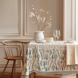 May include: A rectangular tablecloth featuring a repeating pattern of small pine trees in shades of blue, green, and brown on a cream background. The fabric drapes over a table set with a white pitcher, white bowls, and two clear glass flutes.