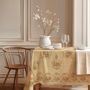 May include: A rectangular beige tablecloth featuring a repeating pattern of pumpkins and ornate floral scrollwork. The table is set with a white ceramic pitcher containing white flowers, two clear glass flutes, and stacked white bowls.