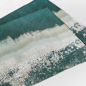 May include: Two teal green placemats with a white and teal green abstract design. The placemats have a speckled texture.