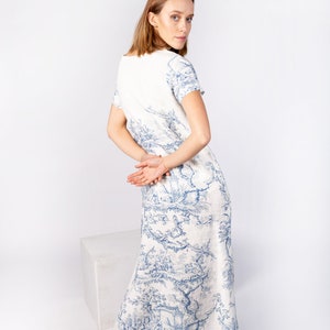 May include: A white linen dress with a blue and white floral print. The dress has a scoop neck and short sleeves. The model is wearing the dress with her hair pulled back.
