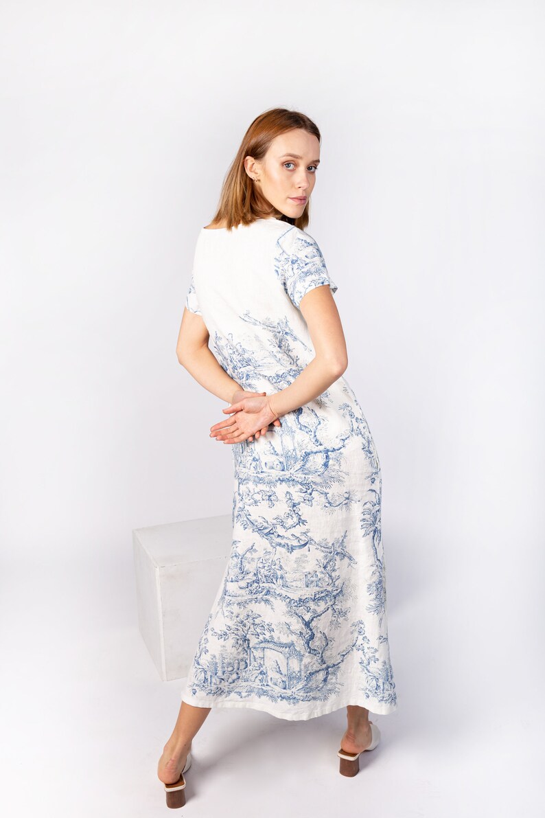 May include: A white linen dress with a blue and white floral print. The dress has a scoop neck and short sleeves. The model is wearing the dress with her hair pulled back.