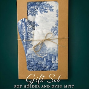 Puede incluir: Un juego de regalo con un agarrador y un guante de horno con un diseño de paisaje azul y blanco. El juego está empaquetado en una caja de cartón marrón y atado con hilo. Las palabras "Gift Set" y "POT HOLDER AND OVEN MITT" están impresas.