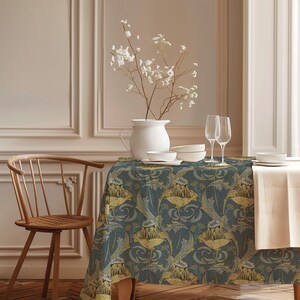 Pode incluir: Uma mesa de jantar coberta com uma toalha de mesa com padrão floral azul-escuro e amarelo. Sobre a mesa, há um jarro branco com flores brancas, duas taças de vinho transparentes e uma pilha de tigelas brancas. Uma cadeira de madeira está próxima.
