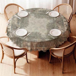 Op de afbeelding: Een ronde eettafel met vier houten stoelen met rugleuningen van gevlochten riet. De tafel is bedekt met een rond tafelkleed met een groen en beige landschapsprint, gedekt met vier witte borden en zilverkleurig bestek.
