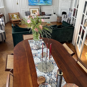 May include: A dining room with a large wooden table, adorned with a floral runner, candles, and decorative bowls. A green velvet sofa and a painting are visible in the background. The room has a classic, elegant aesthetic.