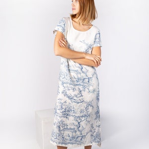 May include: A white linen dress with a blue and white floral print. The dress has a round neckline and short sleeves. The model is wearing white sandals.