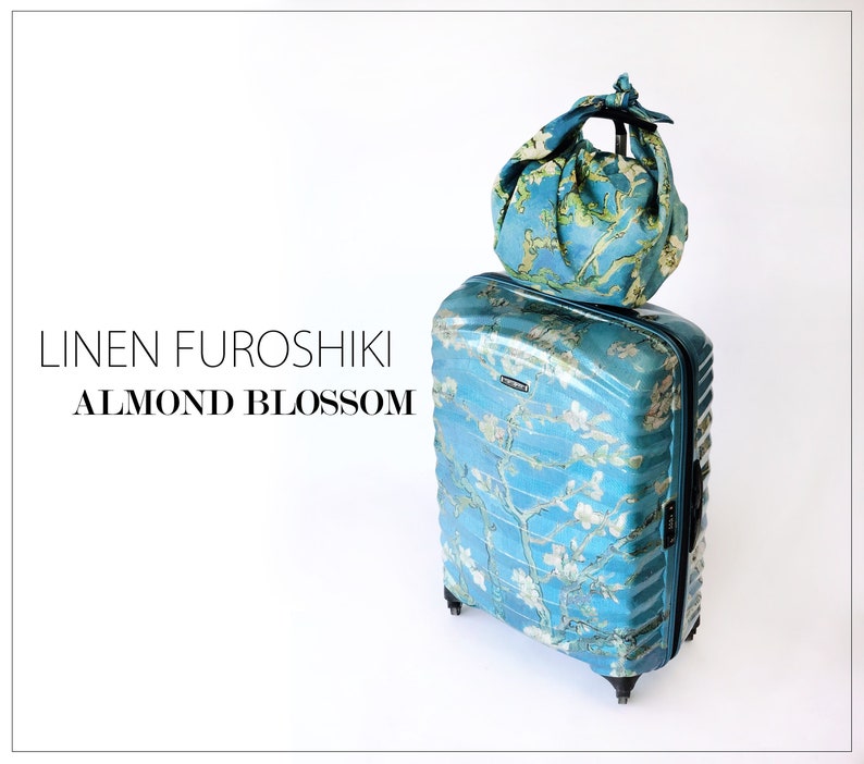 K&ouml;nnte beinhalten: Ein blauer Koffer mit Blumenmuster und eine passende blaue Leinentasche oben drauf. Der Text "LINEN FUROSHIKI ALMOND BLOSSOM" ist auf dem wei&szlig;en Hintergrund gedruckt.