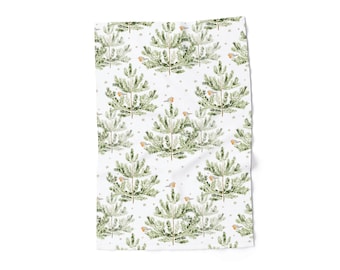 May include: White towel with a repeating pattern of green watercolor Christmas trees, small birds, and tiny gray stars. The towel is folded and has a soft, textured appearance, suitable for kitchen or bathroom use.