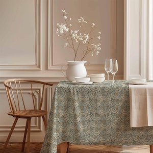 May include: A teal and gold patterned tablecloth with a floral design. The tablecloth is set on a wooden table with a white pitcher, bowls, and glasses. A wooden chair is in the foreground.