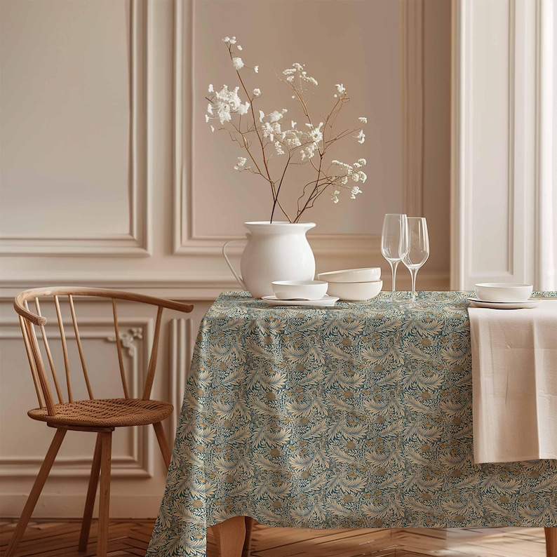 May include: A teal and gold patterned tablecloth with a floral design. The tablecloth is set on a wooden table with a white pitcher, bowls, and glasses. A wooden chair is in the foreground.