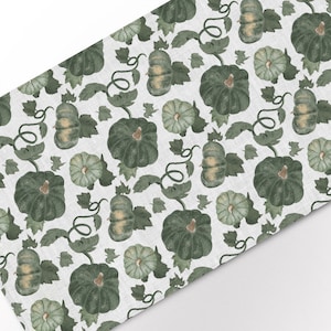 May include: A white fabric table runner with a repeating pattern of green pumpkins and vines. The pumpkins are various shades of green and have a watercolor effect.