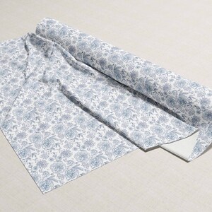 May include: A roll of white fabric with a blue floral pattern. The fabric is folded and rolled up, with the end of the roll visible.