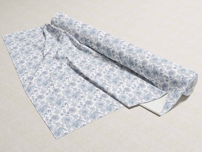 May include: A roll of white fabric with a blue floral pattern. The fabric is folded and rolled up, with the end of the roll visible.
