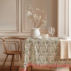 May include: A rectangular tablecloth featuring a repeating pattern of small birds perched on pine branches with green needles and brown cones. The fabric has a cream background and a decorative border with red floral motifs along the bottom edge.
