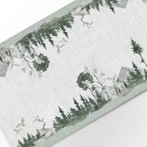 May include: A green and white table runner with a watercolour design of a forest scene. The design features trees, deer, and birds. The runner has a light green border.