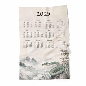 May include: A 2025 calendar printed on a beige linen tea towel with a green snake and bamboo illustration.