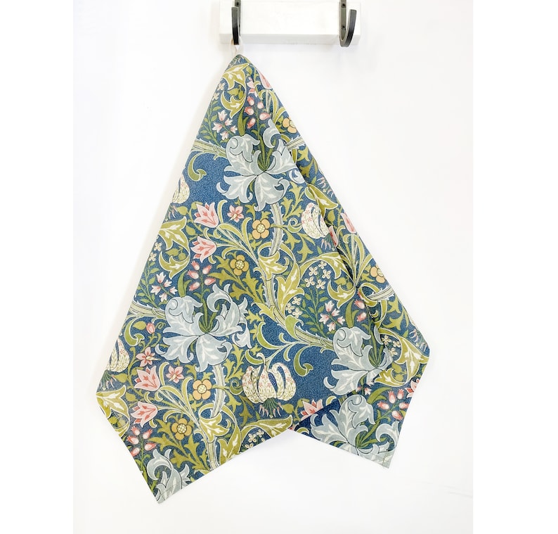 Pu&ograve; includere: Un asciugamano da cucina blu con un motivo floreale che presenta gigli, foglie e piccoli fiori rosa. Il motivo &egrave; in tonalit&agrave; di verde, blu, rosa e giallo.