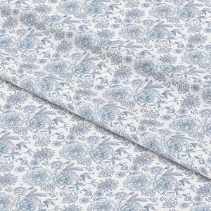 May include: White fabric with a blue floral pattern. The pattern features a variety of flowers, including roses and smaller blooms. The fabric is folded in half, creating a diagonal line.