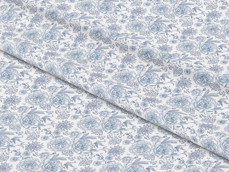 May include: White fabric with a blue floral pattern. The pattern features a variety of flowers, including roses and smaller blooms. The fabric is folded in half, creating a diagonal line.
