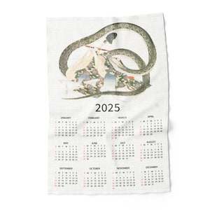 May include: A white tea towel with a 2025 calendar printed on it. The calendar features a traditional Japanese illustration of a woman playing a flute with a snake wrapped around her.