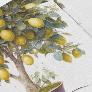 May include: A white linen tea towel featuring a watercolour illustration of a lemon tree with green leaves and yellow lemons. The tree is in a brown pot.