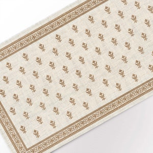 May include: A beige linen table runner with a gold floral pattern. The runner has a decorative border with a repeating design.