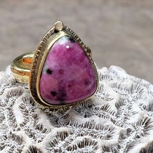 Può includere: Un anello d'oro con una pietra preziosa rosa e nera incastonata in una forma triangolare.