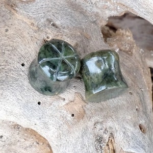 Può includere: Due gauge per orecchie in pietra verde con un designo intagliato. Le gauge sono su una superficie in legno marrone chiaro.