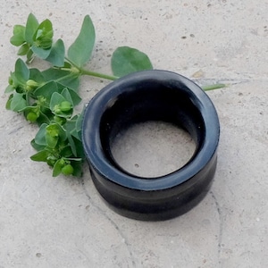 Könnte beinhalten: Ein schwarzer Ohrdehner aus Holz mit glatter, polierter Oberfläche. Der Dehner ist rund und hat einen großen Innendurchmesser.