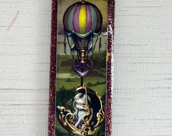 Puede incluir: Imagen rectangular con marco brillante que representa una escena de fantasía. Un globo aerostático a rayas en morado, amarillo y gris flota sobre un paisaje. Debajo, una figura está sentada en una góndola ornamentada. Tema de fantasía.