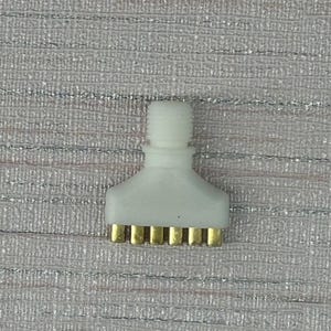 May include: A white plastic component with a threaded top and a wide, flat base. The base has seven gold-coloured pins. The item is set against a textured, silver and white background.