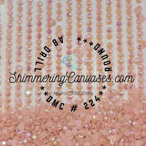 May include: A close-up of a pile of round, iridescent pink diamond-shaped beads. The beads are labeled "*DMC #224*" and "*Approx. 3900 Drills*" and "AB Drill Round *Shimmering Canvases.com*"