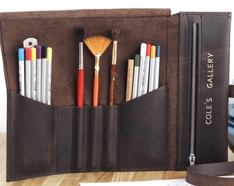 Könnte beinhalten: Eine dunkelbraune Leder-Künstler-Rolltasche, geöffnet zur Präsentation von Kunstzubehör. Die Tasche enthält Buntstifte, Pinsel und einen Bleistift. Der Text "COLE'S GALLERY" ist vertikal auf der Seite mit Reißverschluss der Tasche aufgedruckt.
