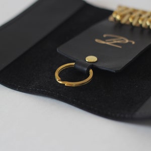May include: Black leather key holder with a gold key ring and a gold metal button. The key holder has a gold embossed letter "P" on the front.