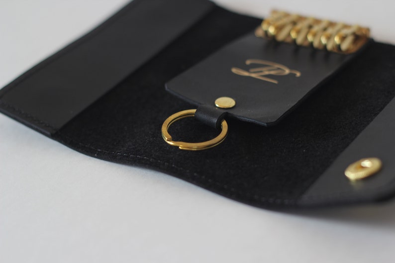 May include: Black leather key holder with a gold key ring and a gold metal button. The key holder has a gold embossed letter "P" on the front.