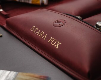 May include: A burgundy leather art supply roll-up case with the text "STARA FOX" in gold lettering. The case is partially open, revealing paint tubes and a paintbrush. The case has a zipper closure and a logo.