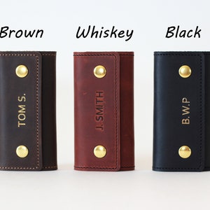 May include: Three leather keychains in brown, whiskey, and black with gold accents. Each keychain has a different name embossed on it: "TOM S.", "J. SMITH", and "B.W.P."