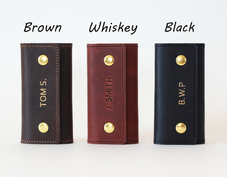 May include: Three leather keychains in brown, whiskey, and black with gold accents. Each keychain has a different name embossed on it: "TOM S.", "J. SMITH", and "B.W.P."