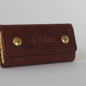May include: A brown leather key holder with a brass chain and two brass buttons. The key holder is embossed with the name "J. SMITH".