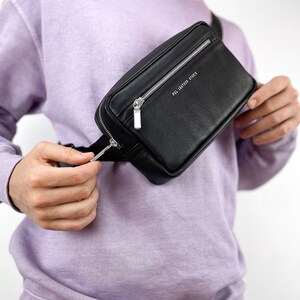 May include: A black leather fanny pack with a silver zipper and the text "POL LEATHER STUDIO" printed on the front.