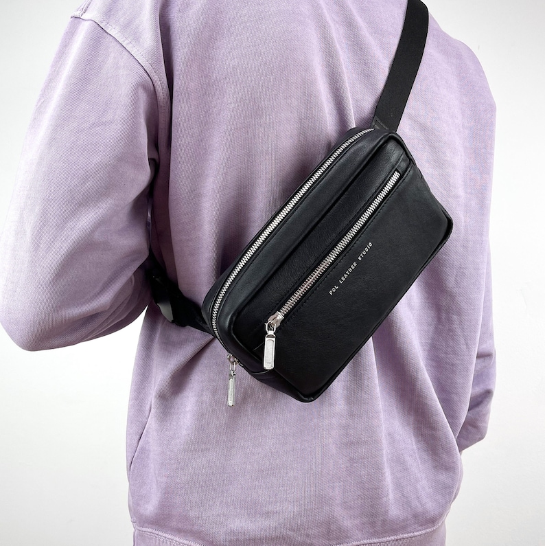 May include: A black leather fanny pack with a silver zipper and the text "POL LEATHER STUDIO" printed on the front.