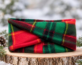 May include: A fleece headband featuring a vibrant red and green plaid pattern with thin yellow accent lines. The fabric is folded in a twisted knot style, creating a layered appearance with a soft, textured surface throughout the entire accessory.
